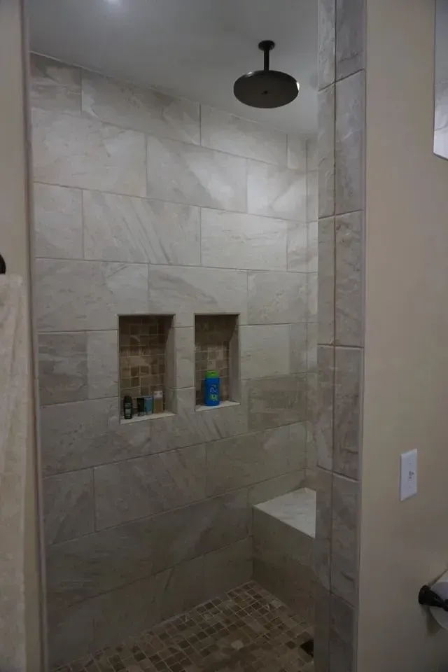 Shower with stone-look tile, built-in bench, two niches, and a rain showerhead.