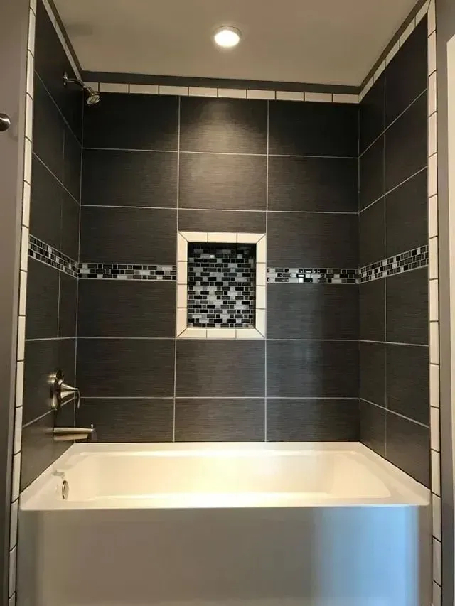 Bathroom with dark gray tiled shower, white bathtub, and recessed shelf with mosaic tiles.