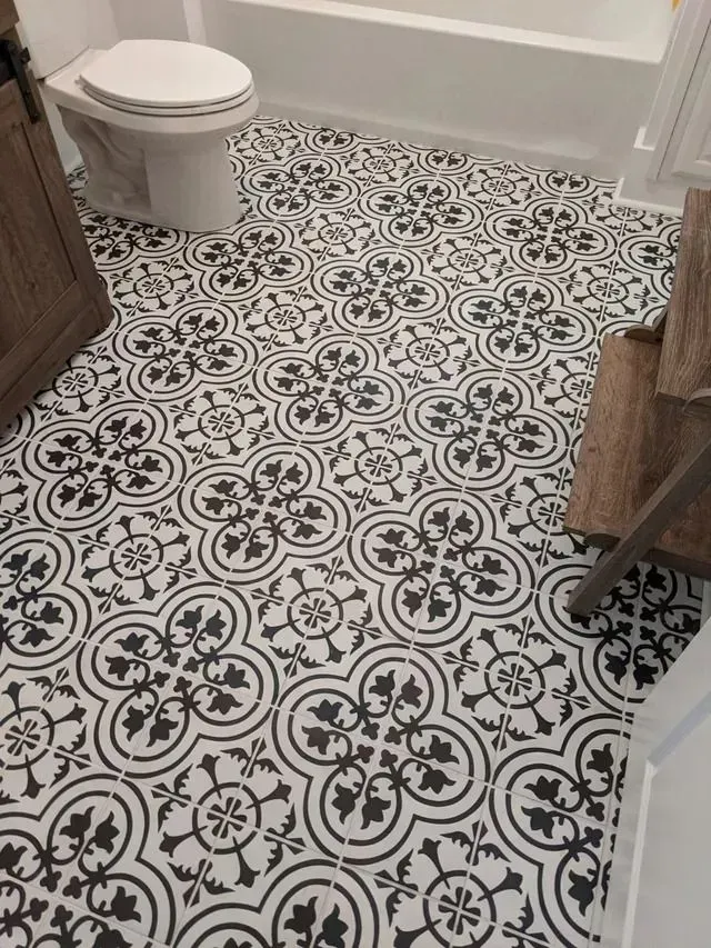 Black and white patterned tile flooring in a bathroom. Toilet and wooden furniture in view.
