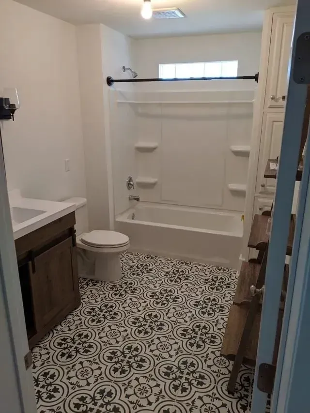 Bathroom with patterned floor, white fixtures, and brown vanity.