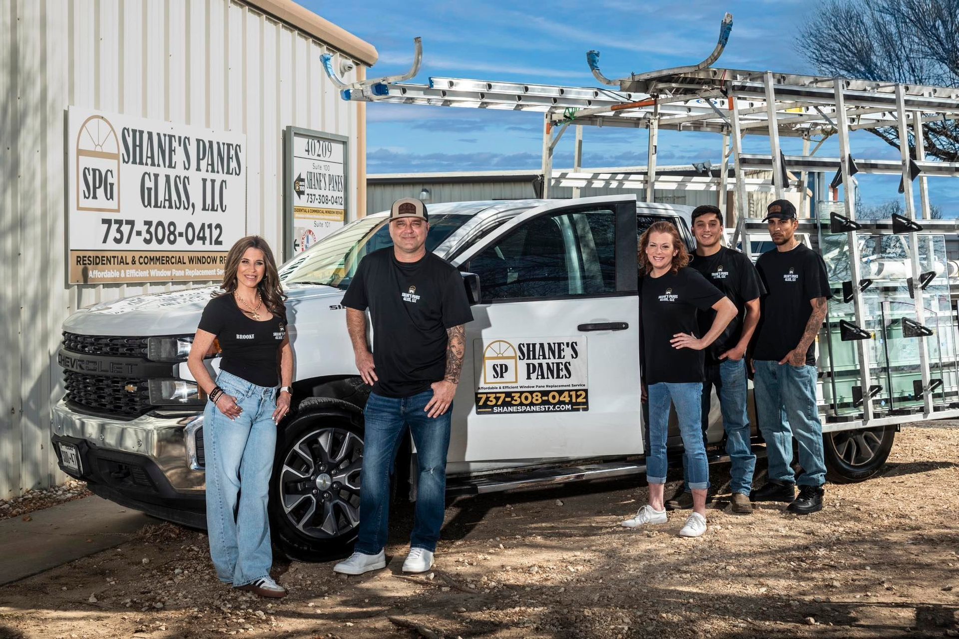 Five people stand by a white truck with glass racks. Sidney's Glass logo on truck and building. Blue sky.