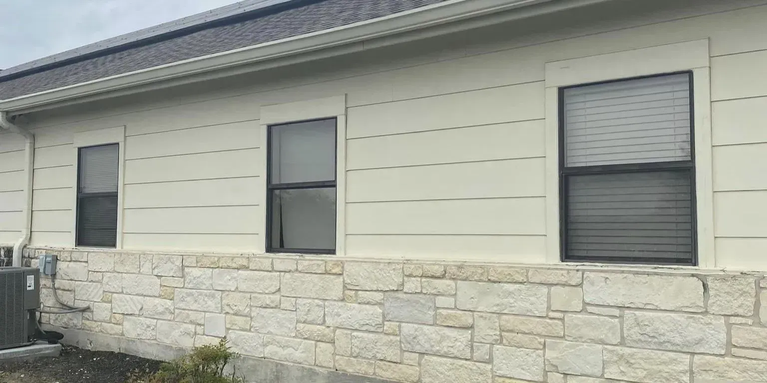 Exterior wall with three windows and a stone veneer base.