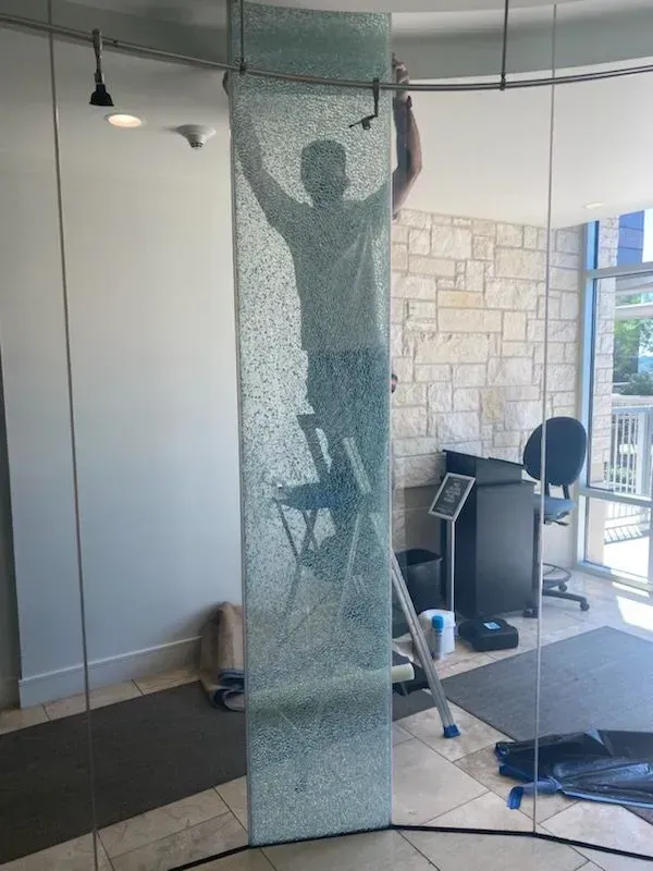 Person on a ladder installing a decorative glass panel in a building.