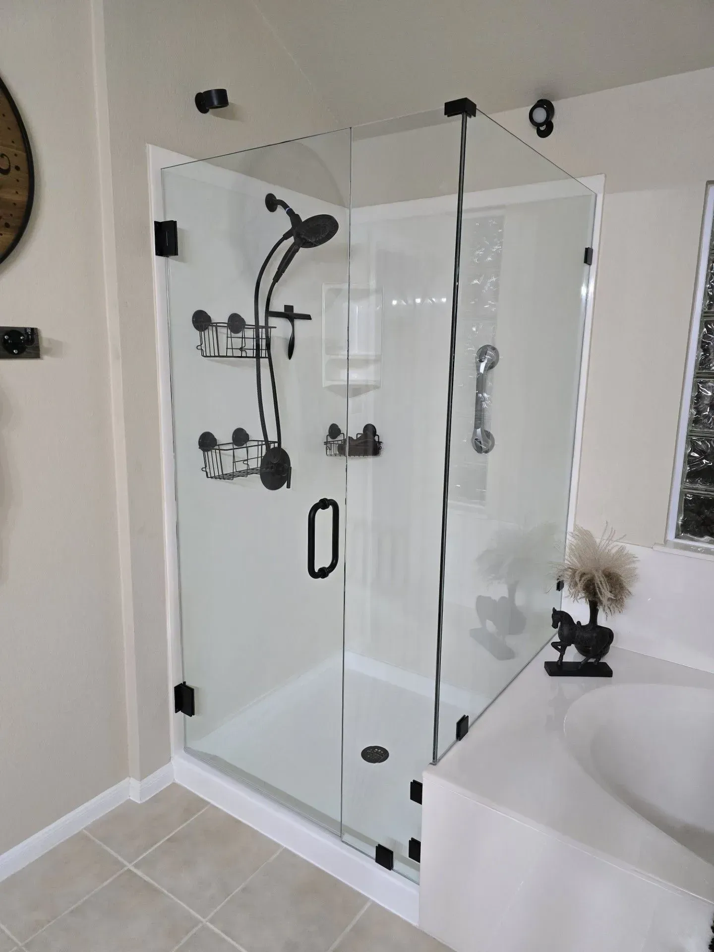 Glass shower enclosure with black fixtures and white walls.