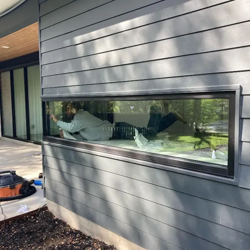 A person working on a long, rectangular window set in gray siding.