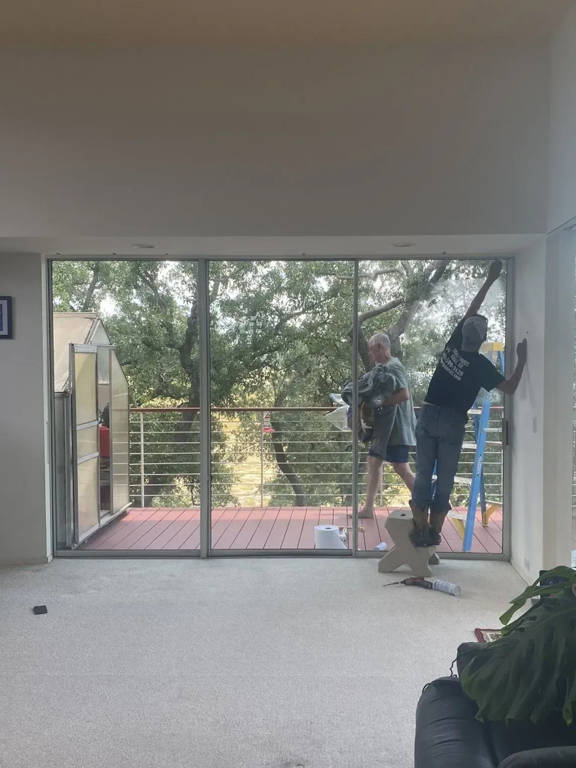 Three people inside, one balancing. Sliding glass door overlooks a deck and trees. Interior is light colored.