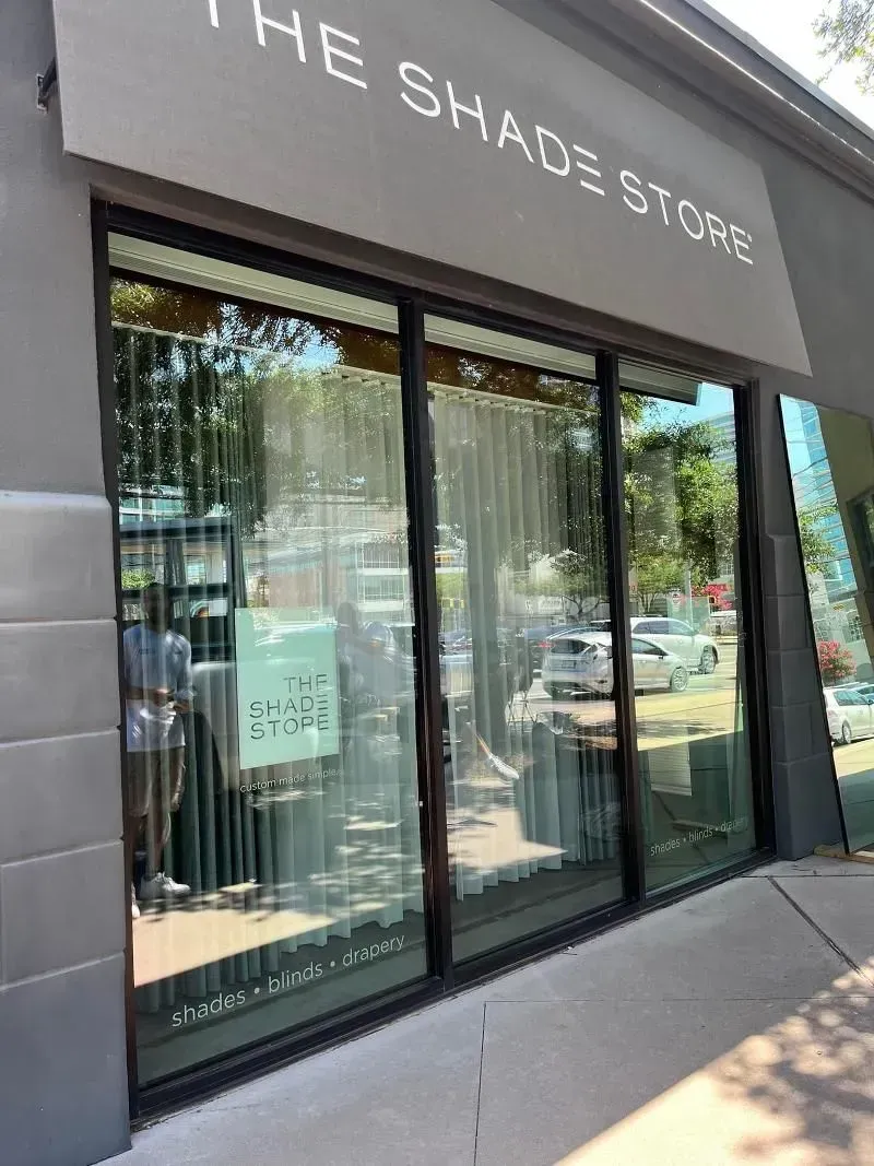 The Shade Store storefront with large windows reflecting outdoor scene; gray facade and sign.