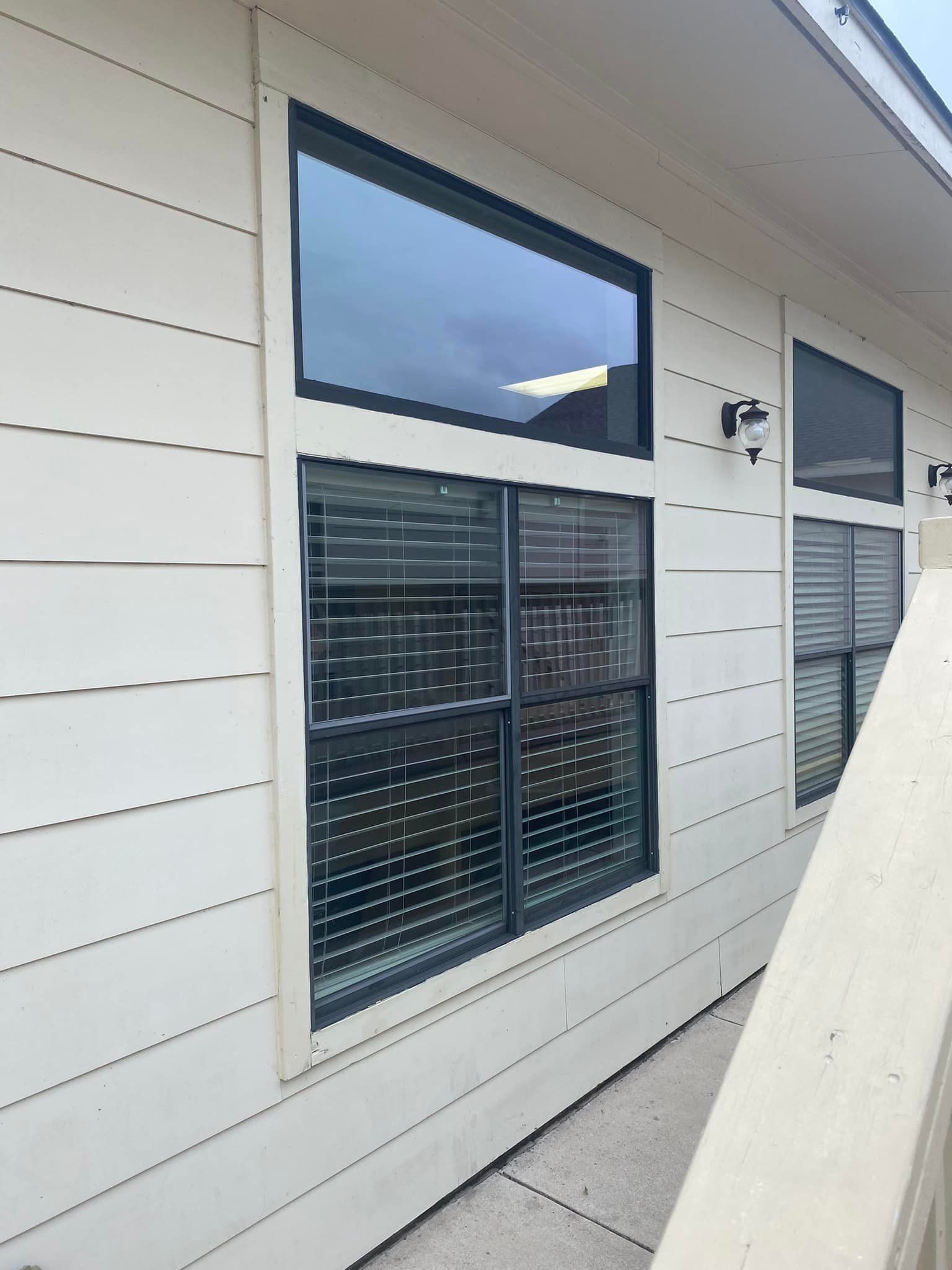 Exterior view of a building with cream siding and black-framed windows, some with blinds, and black exterior lights.