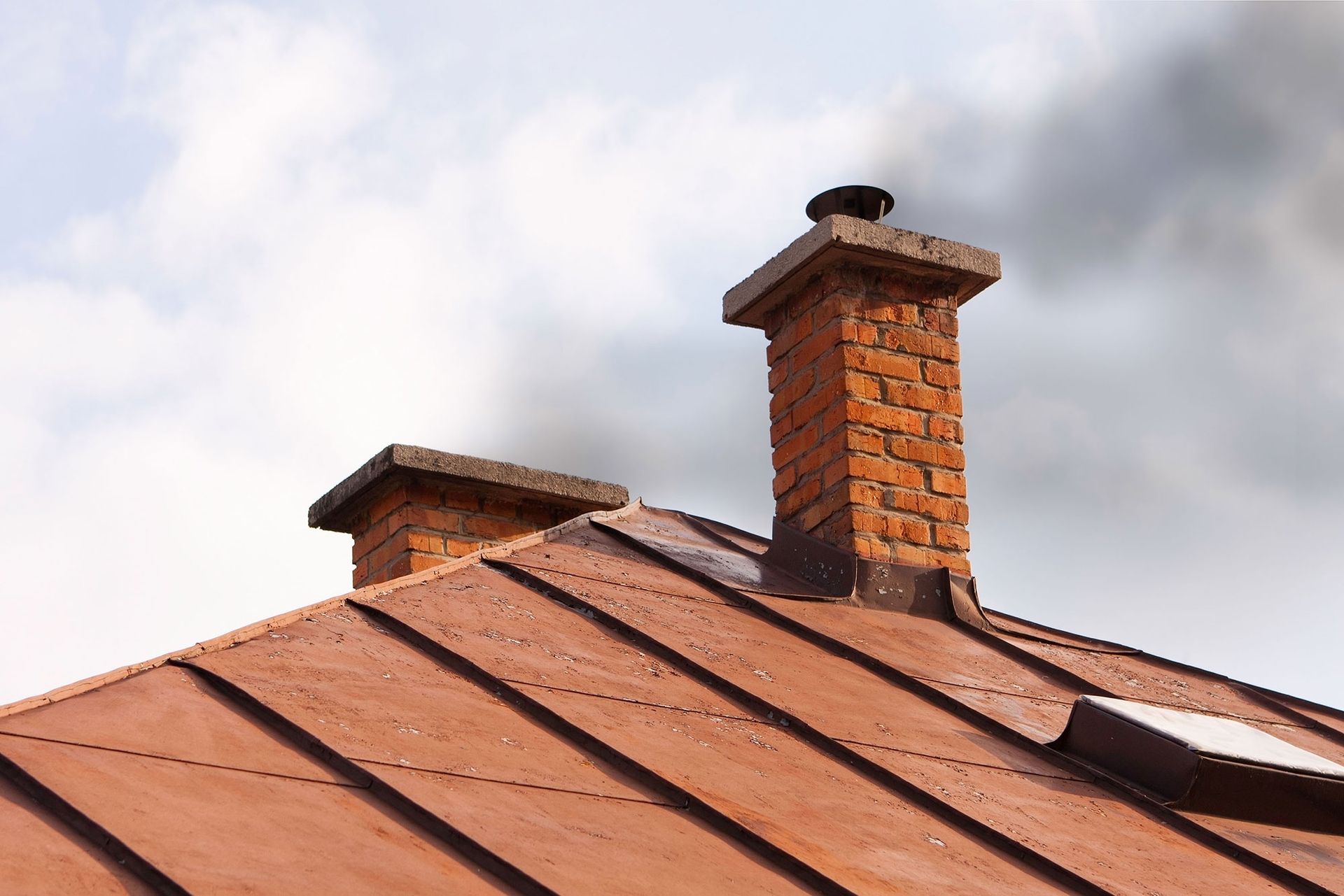 Rooftop with orange metal panels and brick chimneys against a cloudy sky