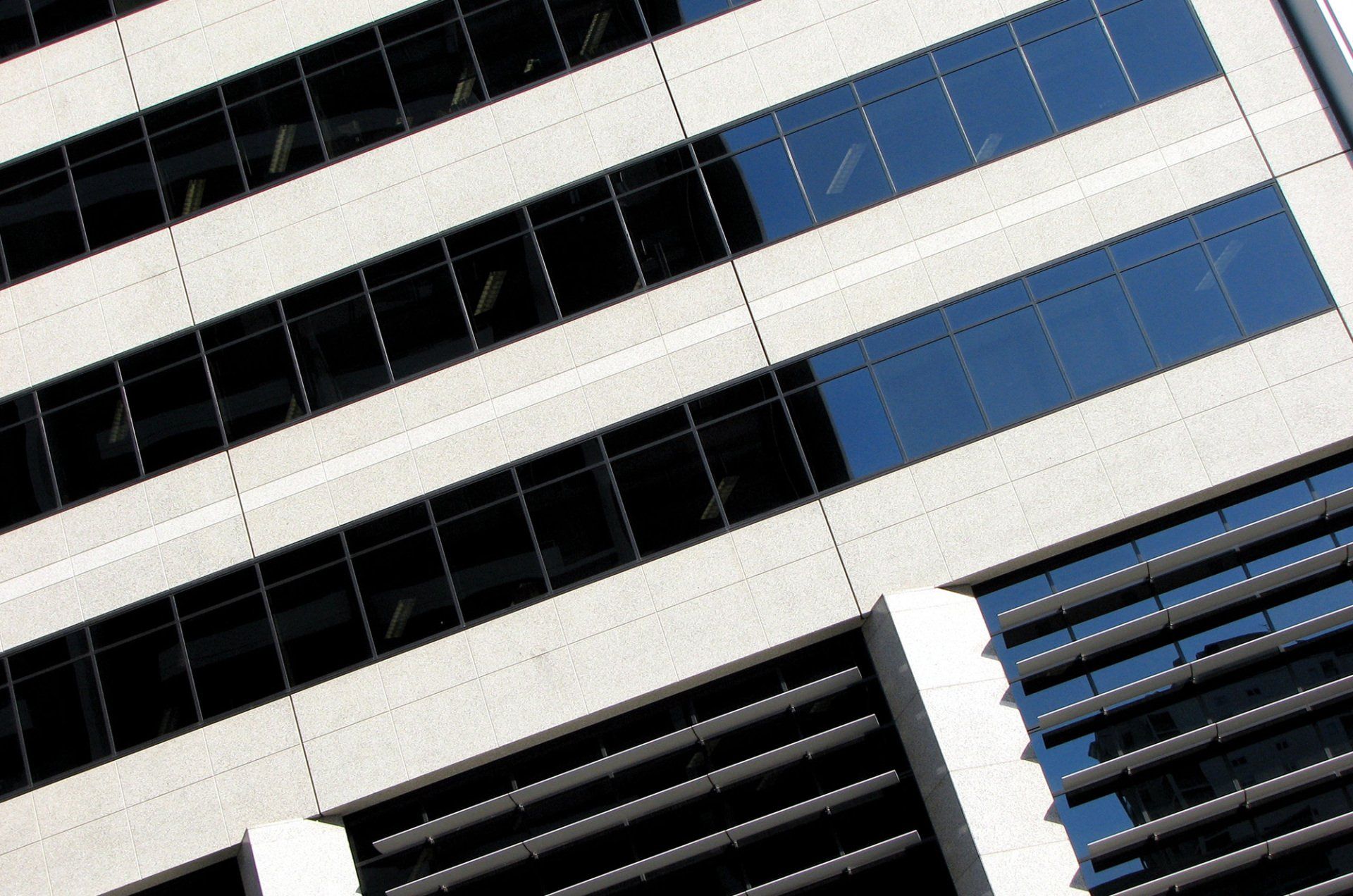 A low-angle view of a modern office building with rows of rectangular glass windows and white stone siding.