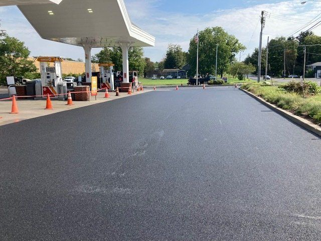 Freshly paved gas station lot with pumps under a canopy. Orange cones line the edge.