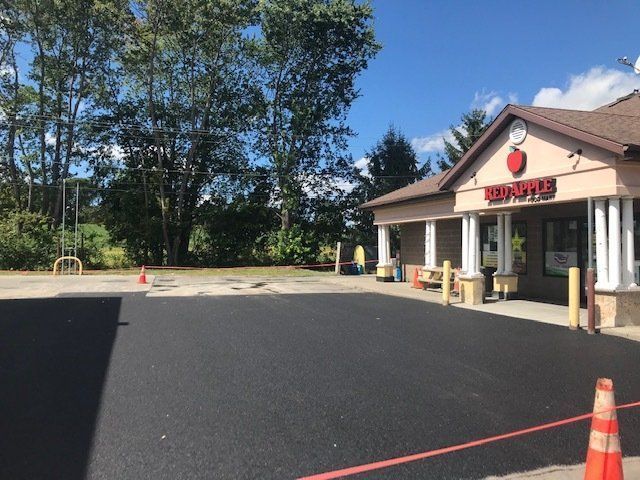 Exterior view of a Red Apple store with a newly paved asphalt parking lot on a sunny day.