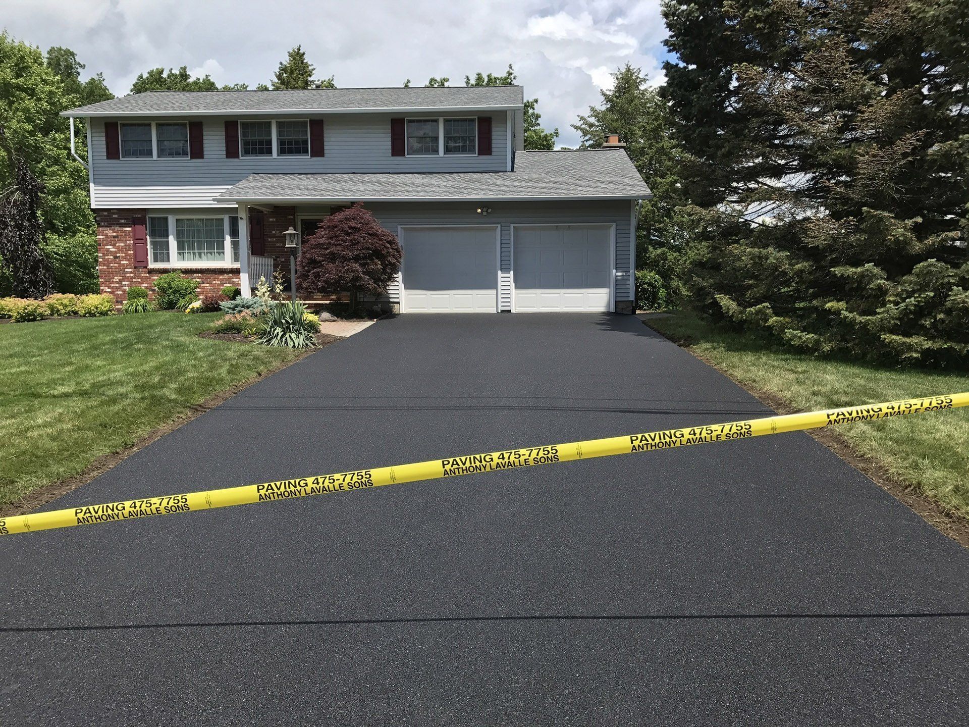 Two-story house with newly paved black driveway. Yellow caution tape across driveway.