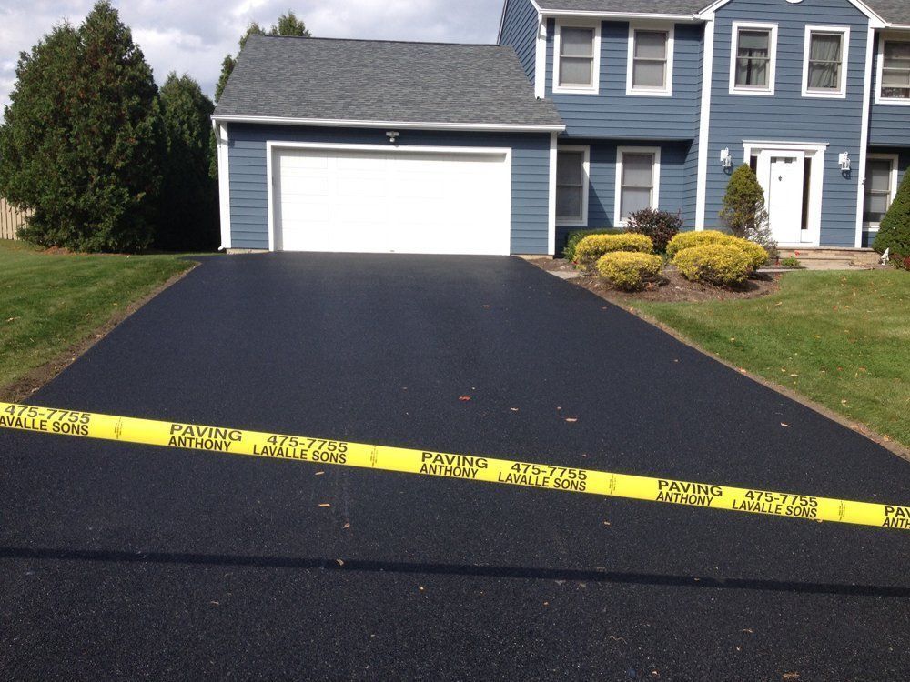 Freshly paved black asphalt driveway leading to a blue house with white garage door and yellow caution tape.