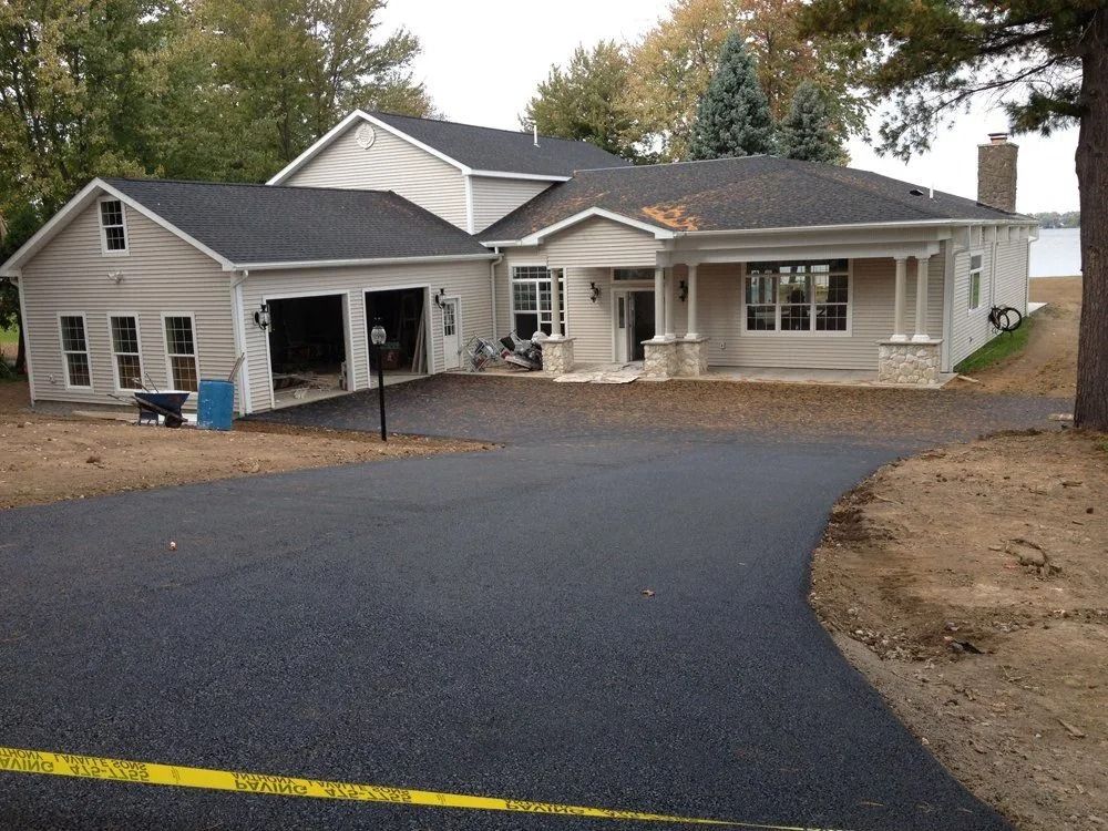Asphalt driveway leads to a stucco house with a two-car garage. Yellow caution tape in foreground.