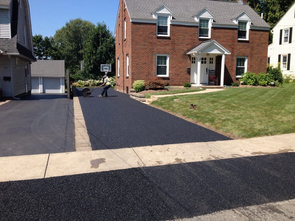Newly paved asphalt driveway in front of a brick house with a person sealing the edges.