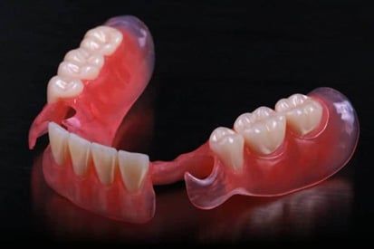 A close up of a denture with teeth on a black background.