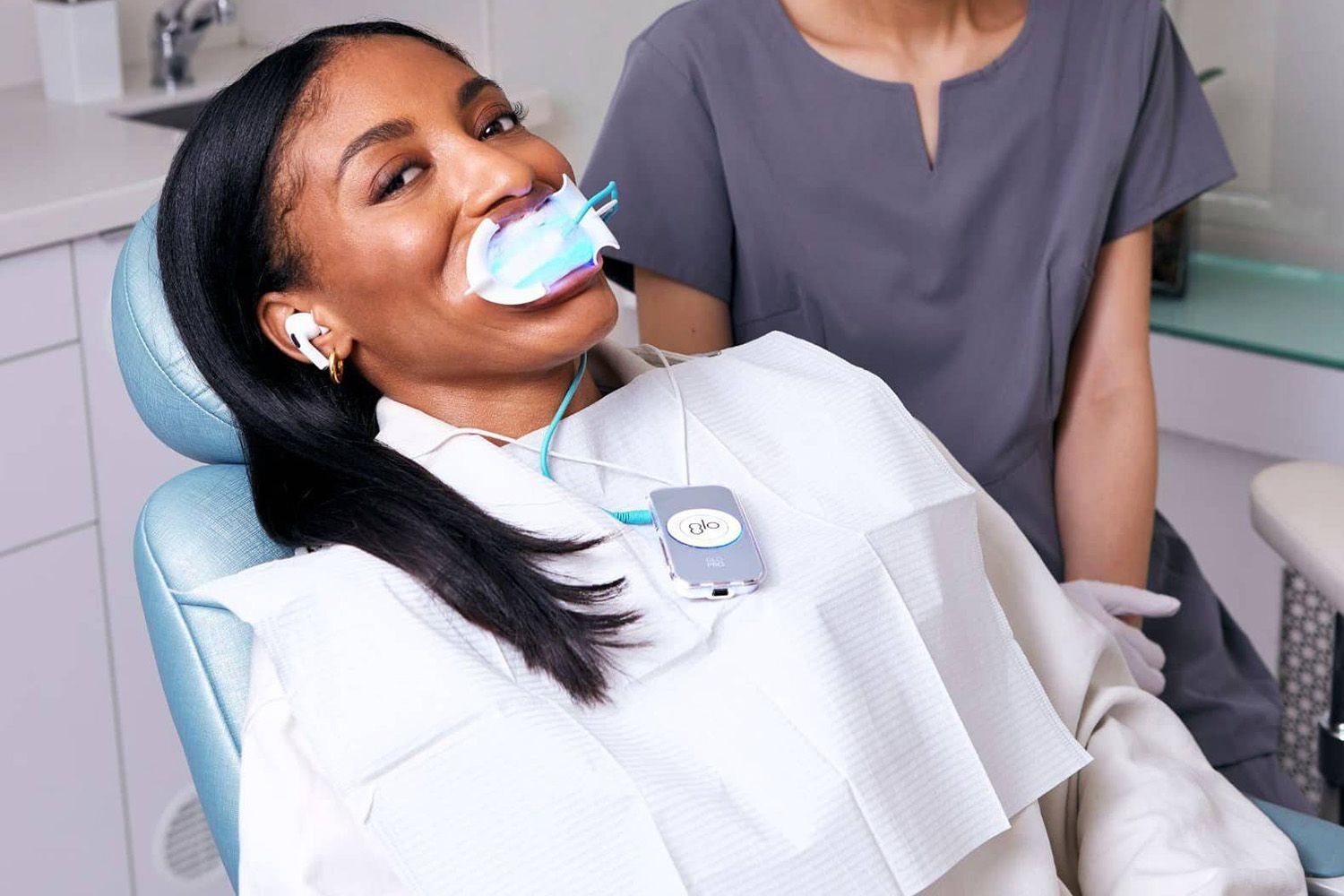 A woman is sitting in a dental chair with a toothbrush in her mouth.