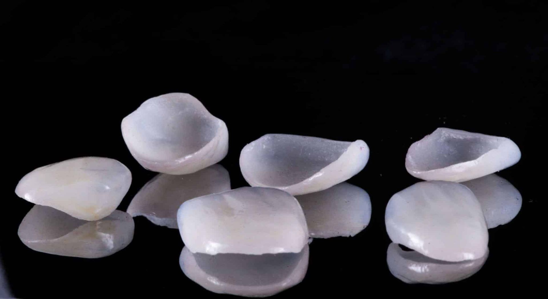 A group of dental crowns are stacked on top of each other on a black surface.