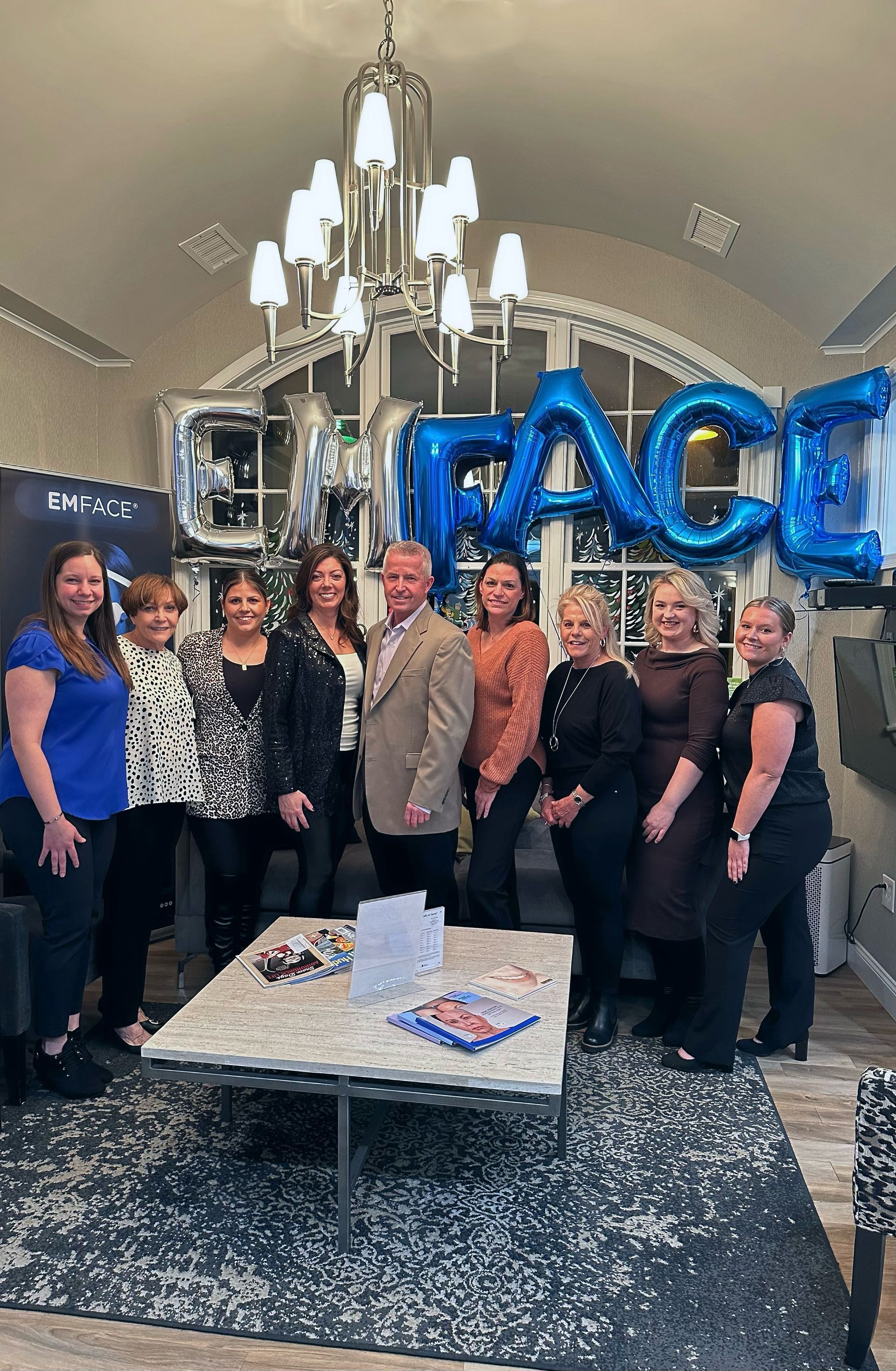 A group of people are posing for a picture in a living room with blue balloons.