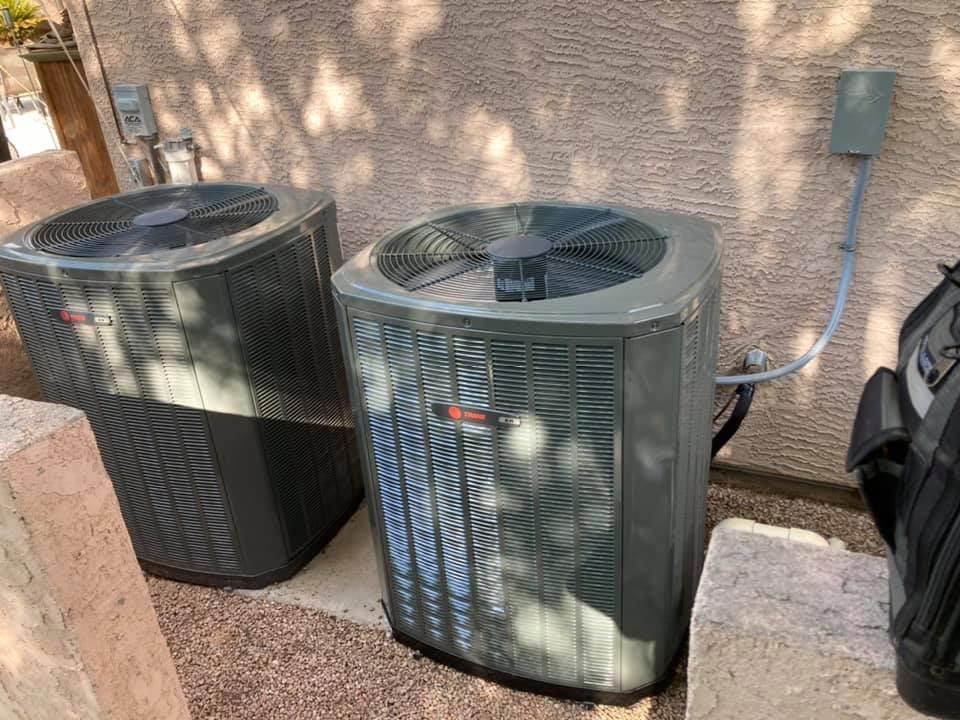 Two air conditioners are sitting next to each other on the side of a building.