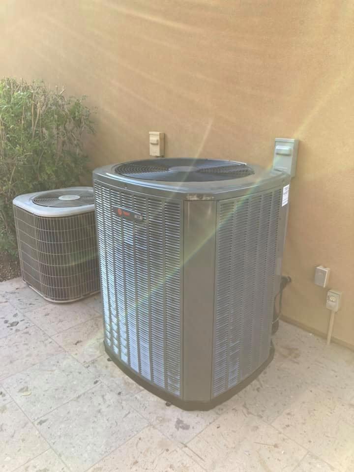 Two air conditioners are sitting next to each other on the side of a building.