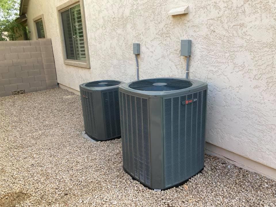 Two air conditioners are sitting on the side of a house.