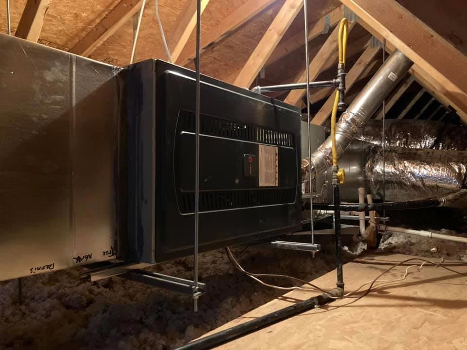 An attic with a lot of pipes and ducts hanging from the ceiling.