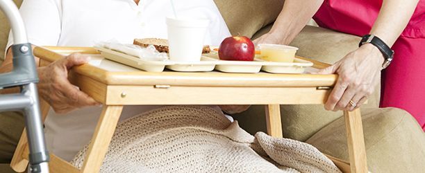 Person being served a meal on a tray while seated. Another person assists with tray on lap.