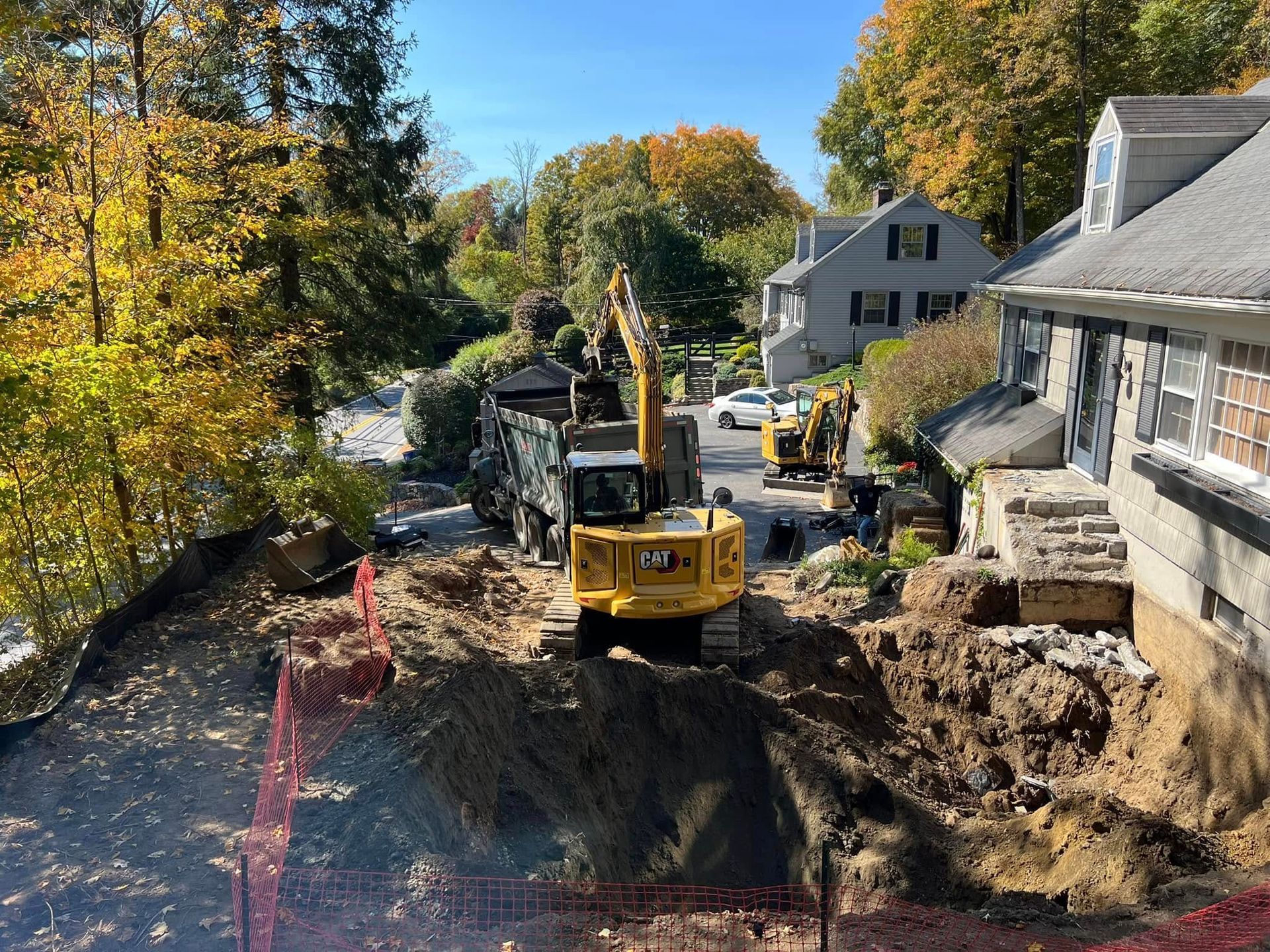 A yellow excavator loads dirt into a dump truck next to a residential house during a construction project.