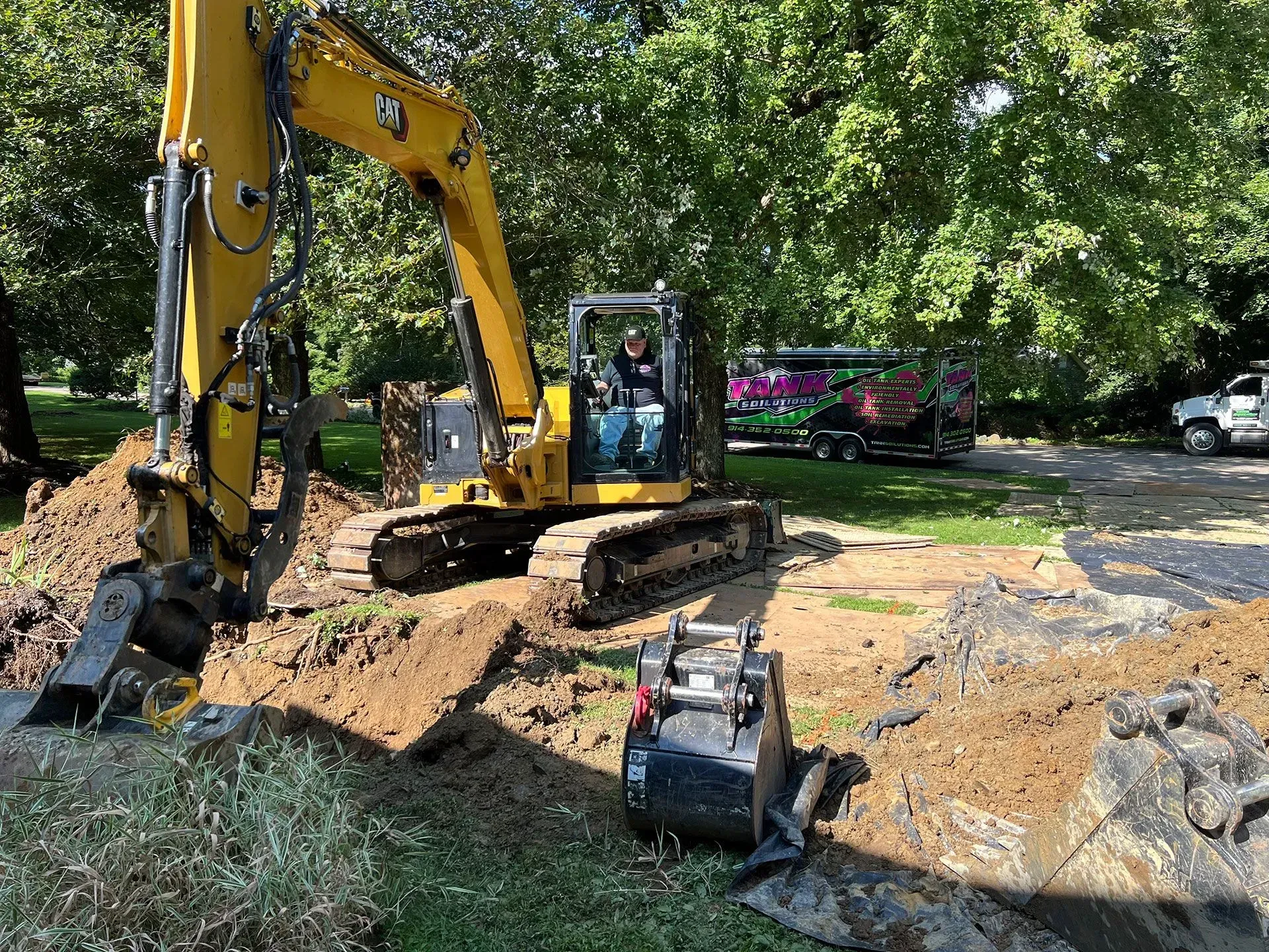 A yellow excavator sits in a grassy area next to a trench, with a detached piece of construction equipment in the dirt.