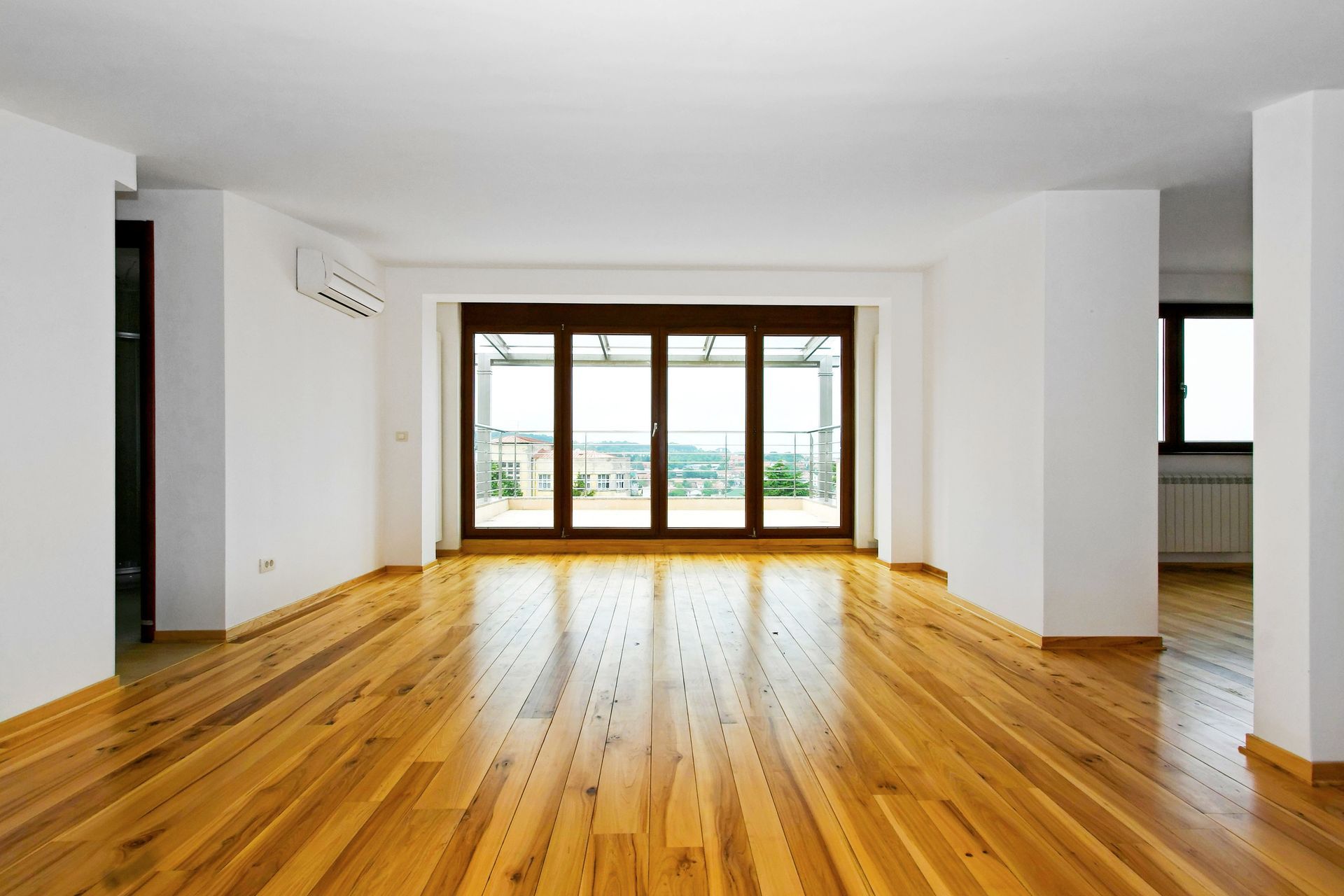Empty room with wood floors, large windows, and white walls.