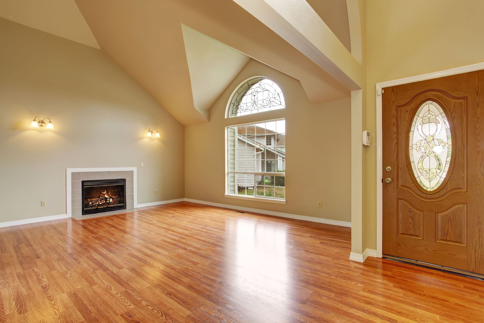 Empty living room with hardwood floors, fireplace, arched window, and wooden door.