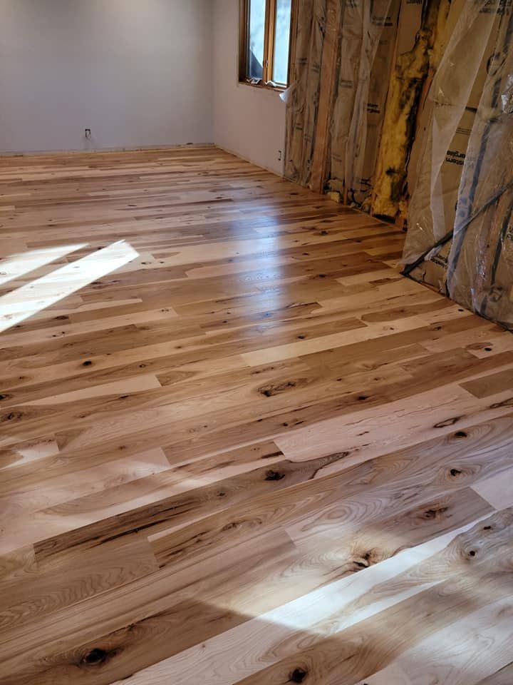 Hardwood floor in a room with white walls, and a window with sunlight shining.