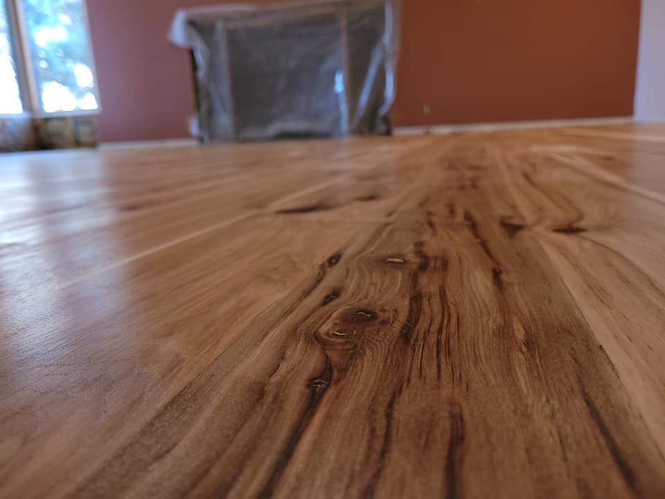 Close-up of polished hardwood floor, with wood grain visible. Brown walls and a covered object are in the background.