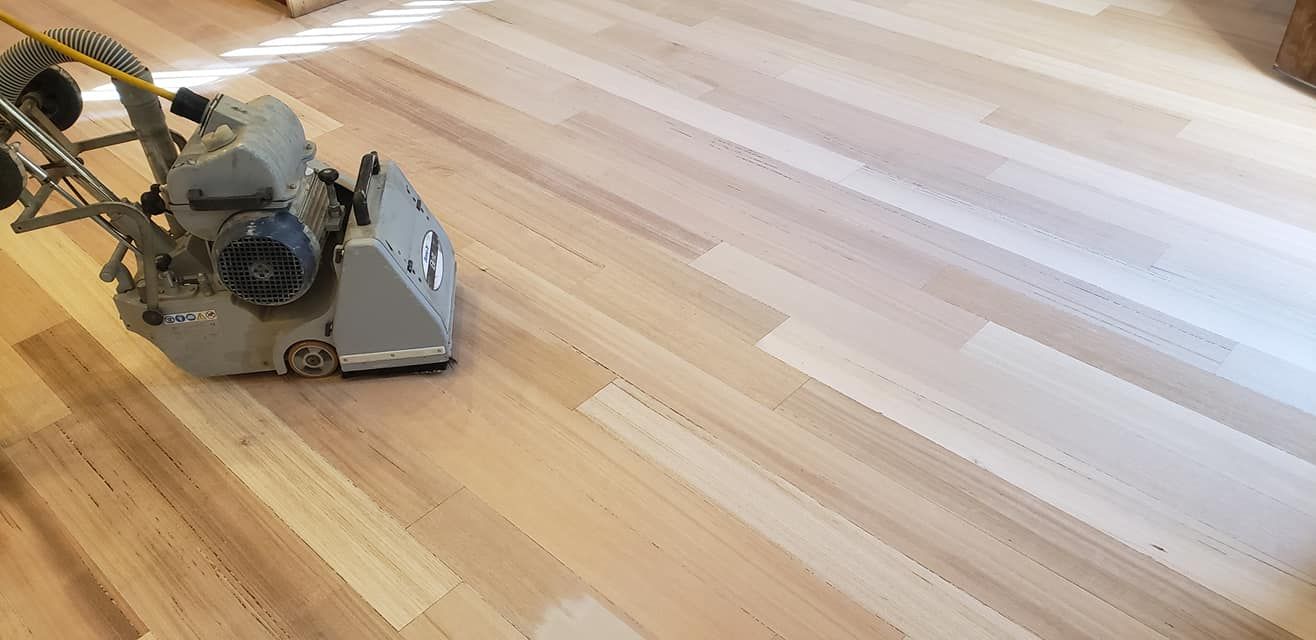 A floor sander in use on a light-colored wooden floor.