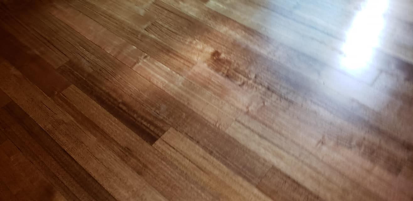 Wooden floor with visible grain and glossy finish; some cracks present.