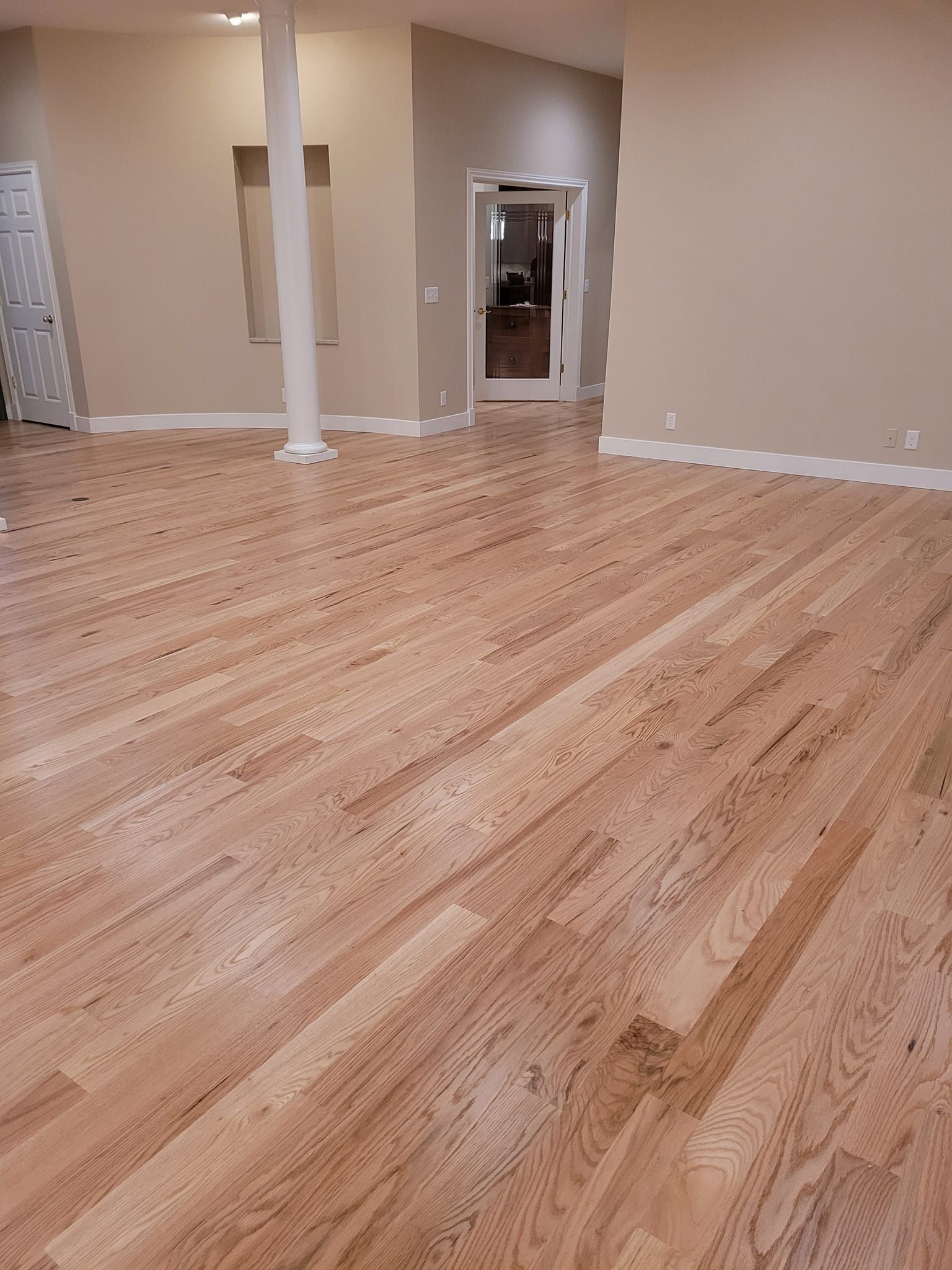 Hardwood flooring in a room with neutral walls, doorway, and support column.