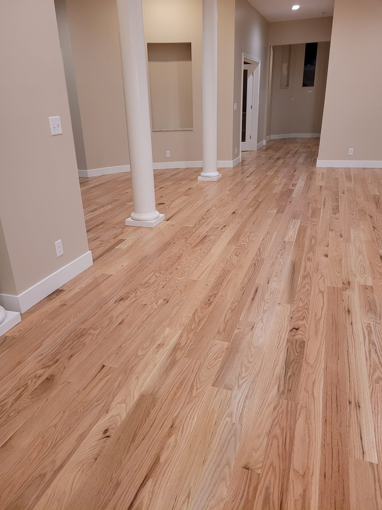 Hardwood floor in a room with white columns, beige walls, and doorways.