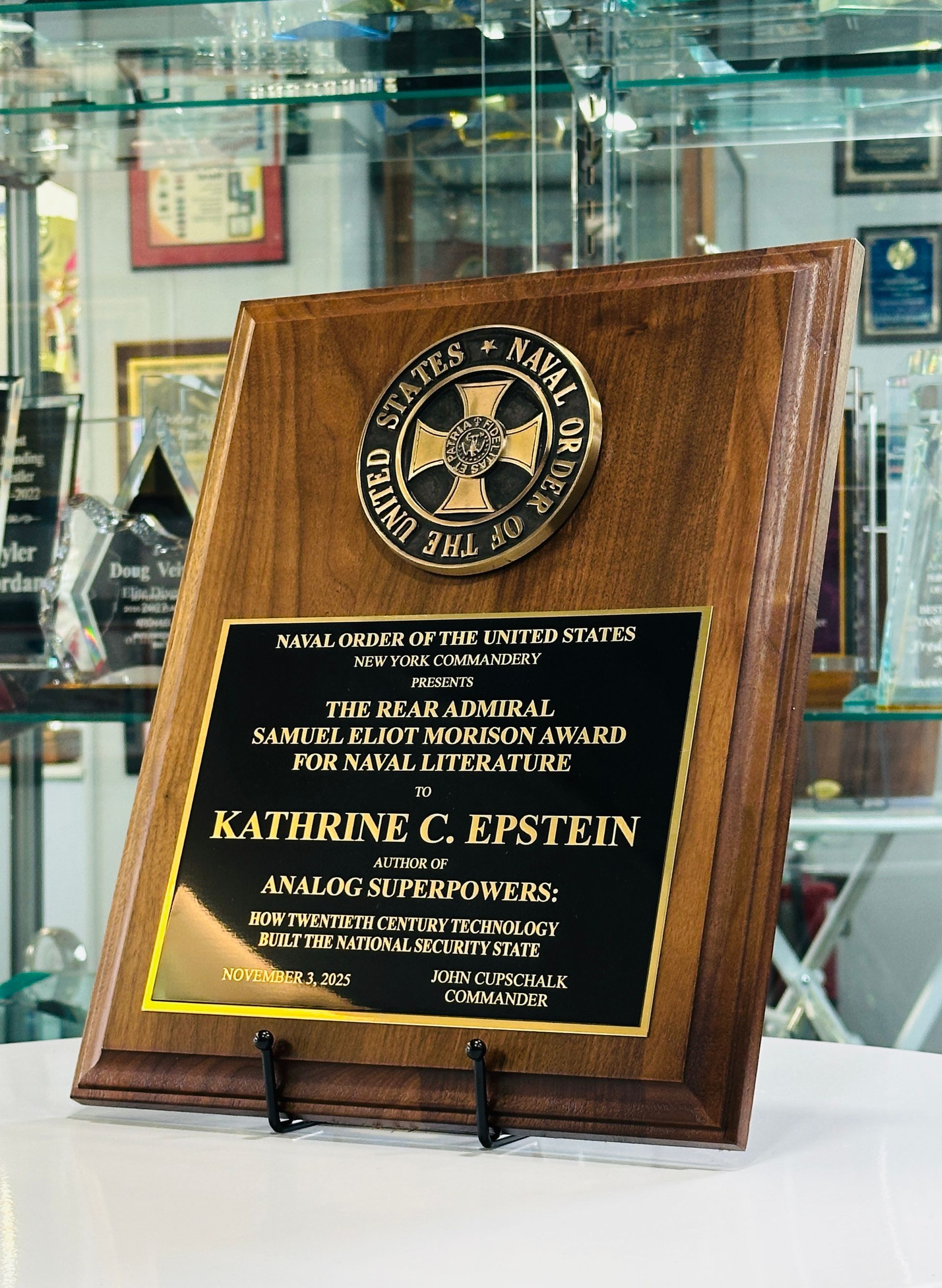 Wooden plaque with gold text and a circular seal, awarded to Katherine C. Epstein for service.