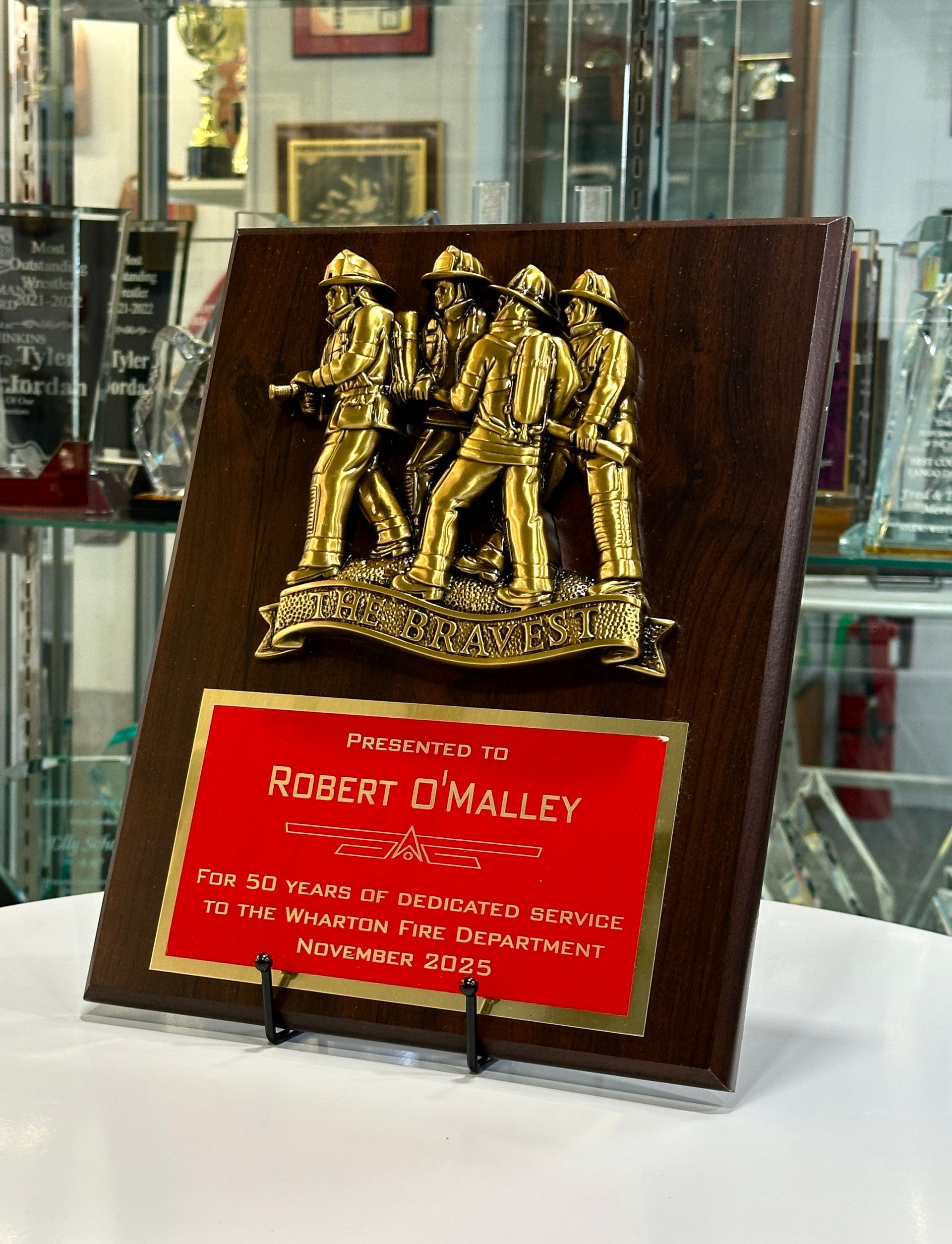 Plaque with golden firefighters statue on a wooden background. Red plate reads
