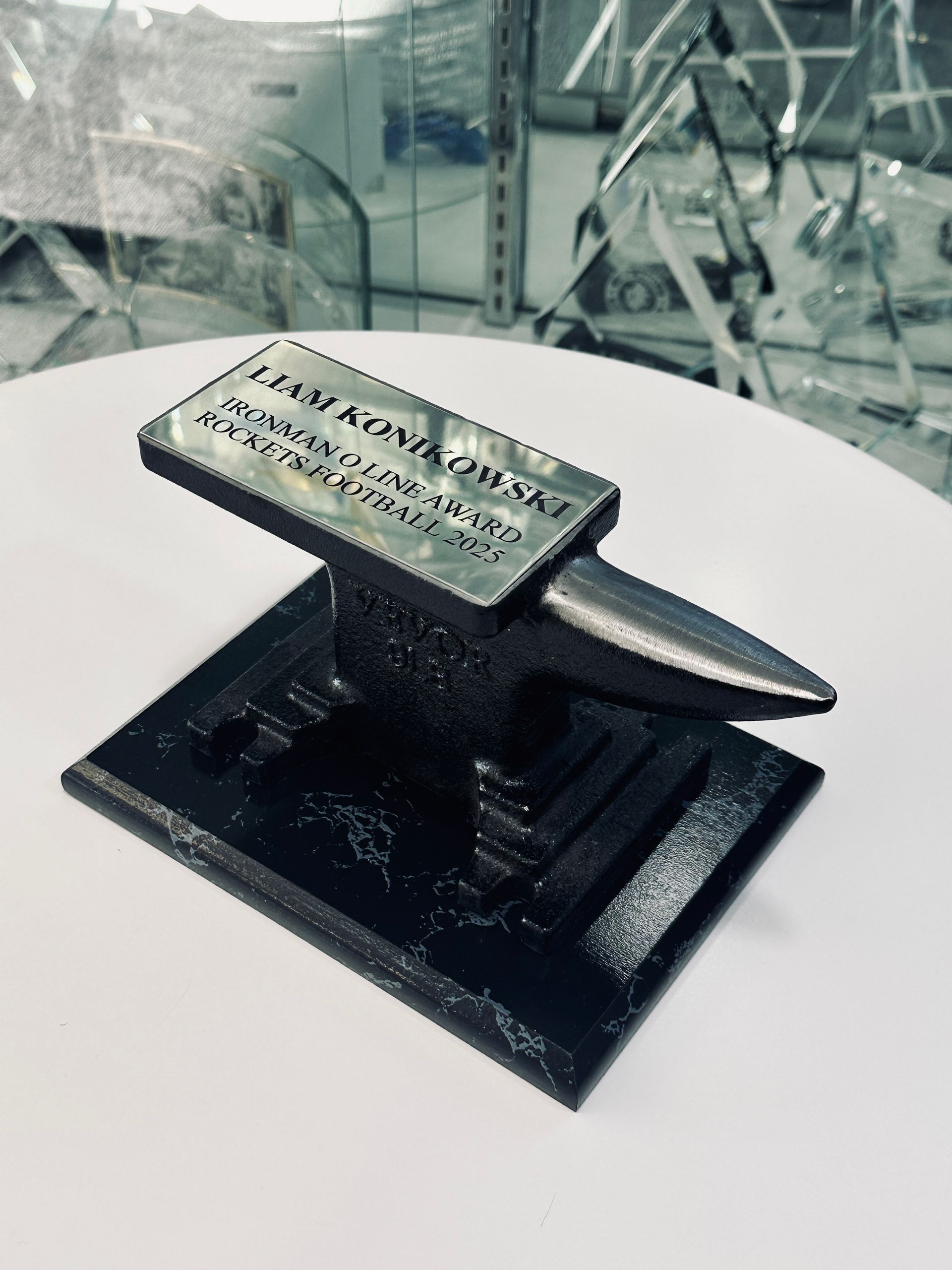 Miniature black anvil with a plaque on a white table.