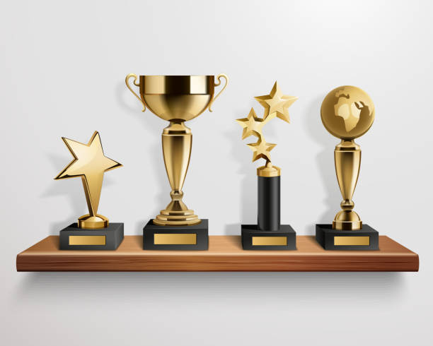 Golden trophies on a wooden shelf, against a white wall.