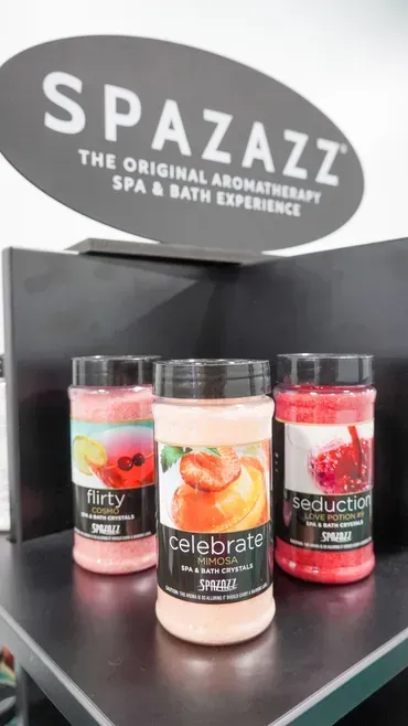 Spa display with three scented candles on a black shelf beneath a “SPAZAZZ” sign.