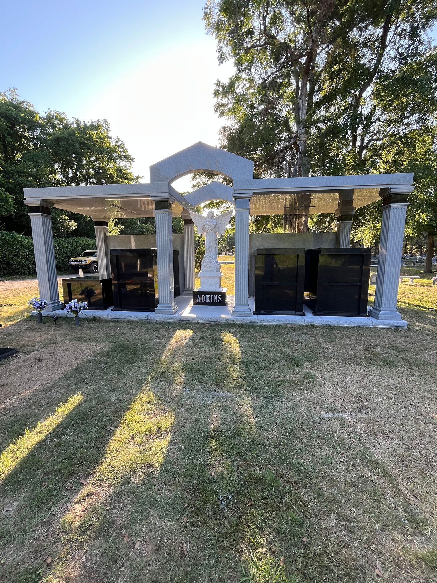 Stone mausoleum in a cemetery with an angel statue and dark burial chambers.