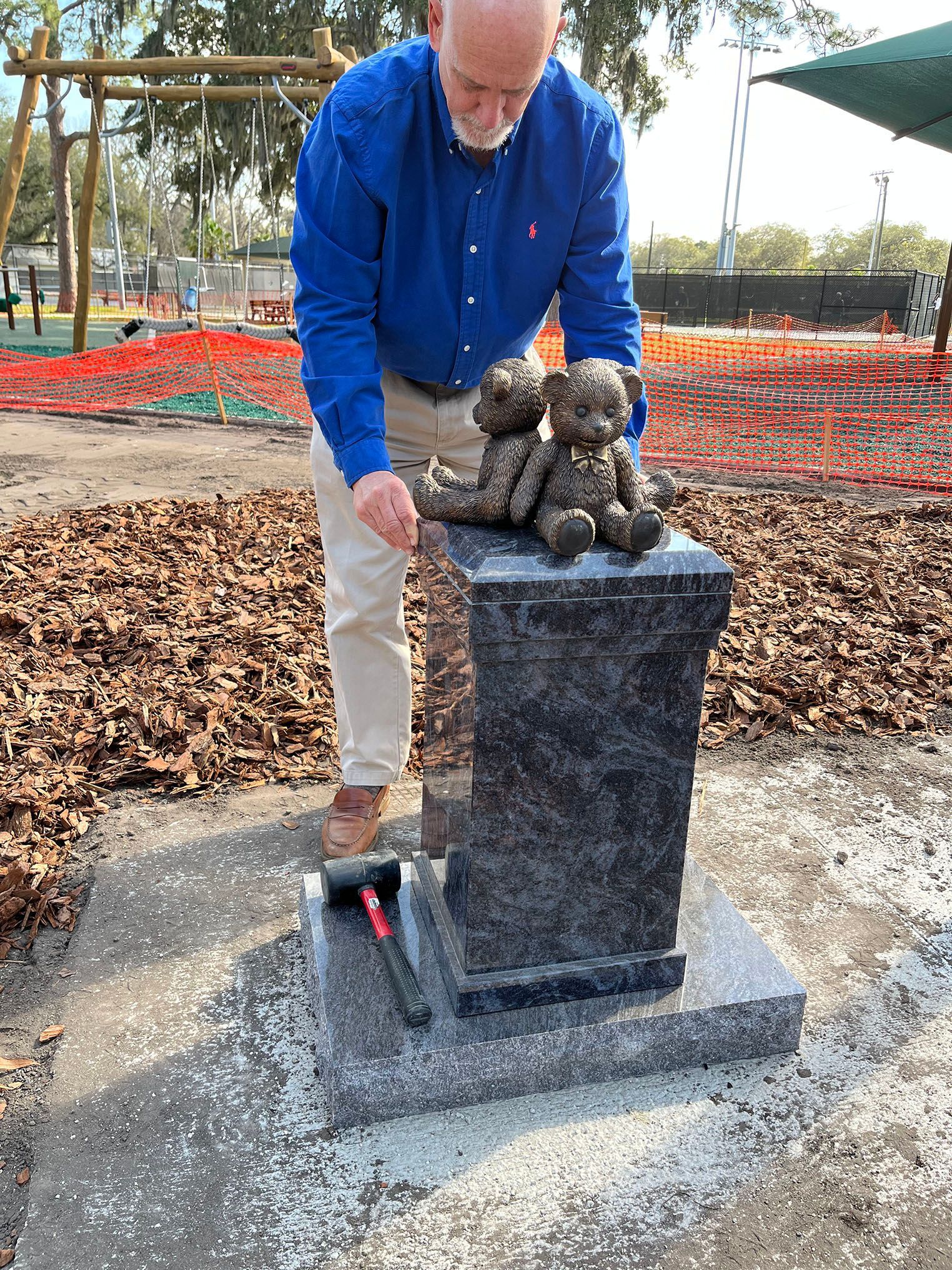 Man placing a small bear statue on a stone monument in a park.