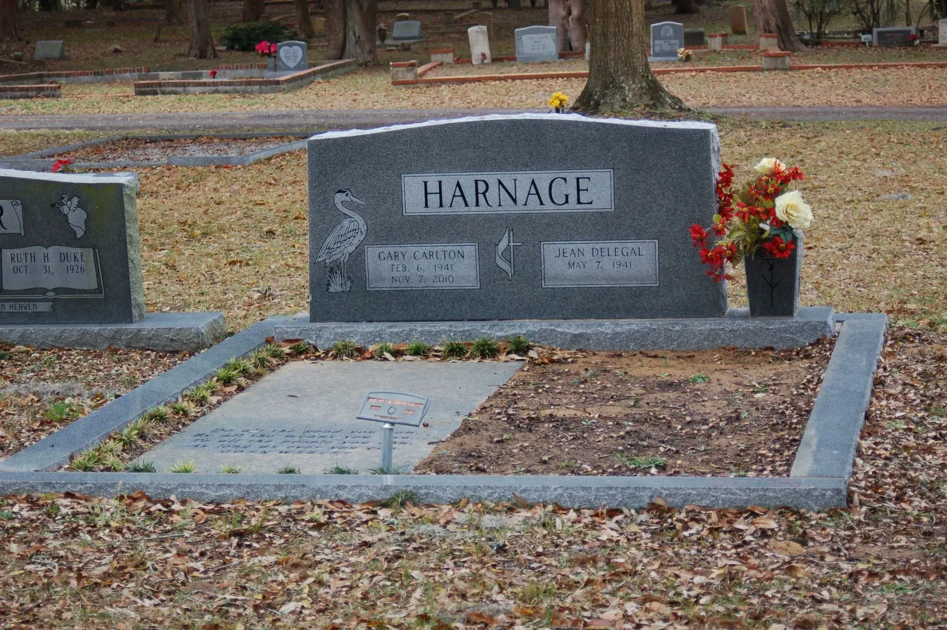 Grave with headstone and the name HARNAGE. Includes flowers in a vase and a stone border.