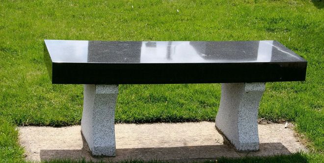 Black granite bench with light-colored, stone-textured legs on a grassy area.