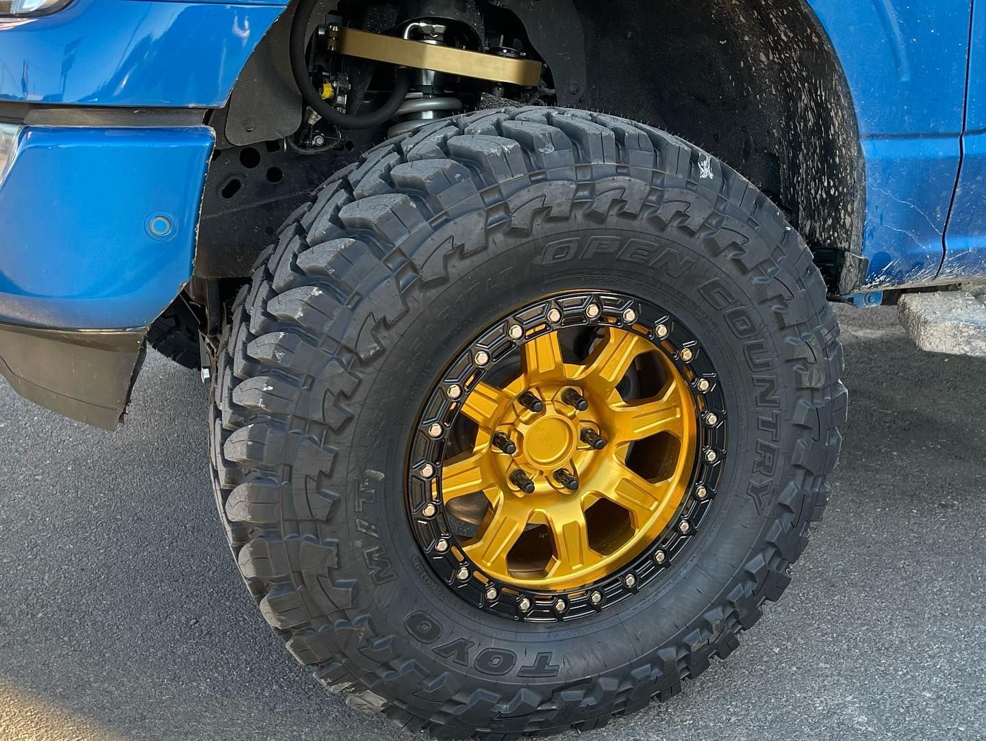 A blue truck with gold rims and tires is parked on the side of the road.