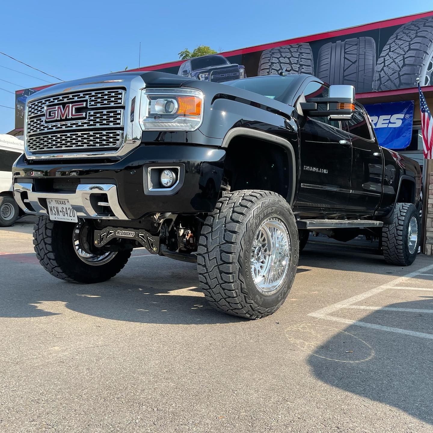 A black gmc truck is parked in front of a tire store.